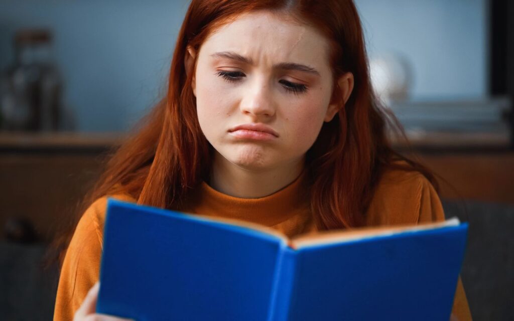 woman in an orange sweater reading a book she doesnt like